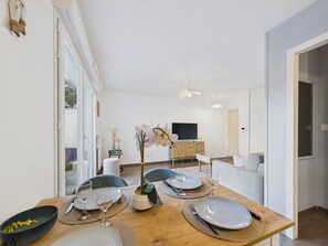 A dining area with a wooden table set for four, a television in the background, and a modern interior design. - Apartment for 2 adults/2 kids near Grande Plage (Les Sables-d´Olonne)