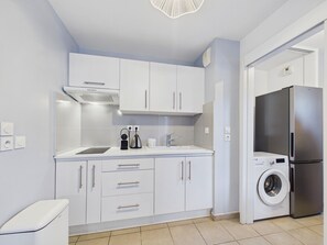 Eine moderne Küche mit weißen Schränken, einem eingebauten Backofen, einem Edelstahlkühlschrank und einer Waschmaschine.
