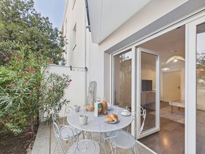 An outdoor dining area with a table and chairs, a glass door leading to an interior space, and a potted plant with pink flowers. - Apartment for 2 adults/2 kids near Grande Plage (Les Sables-d´Olonne)