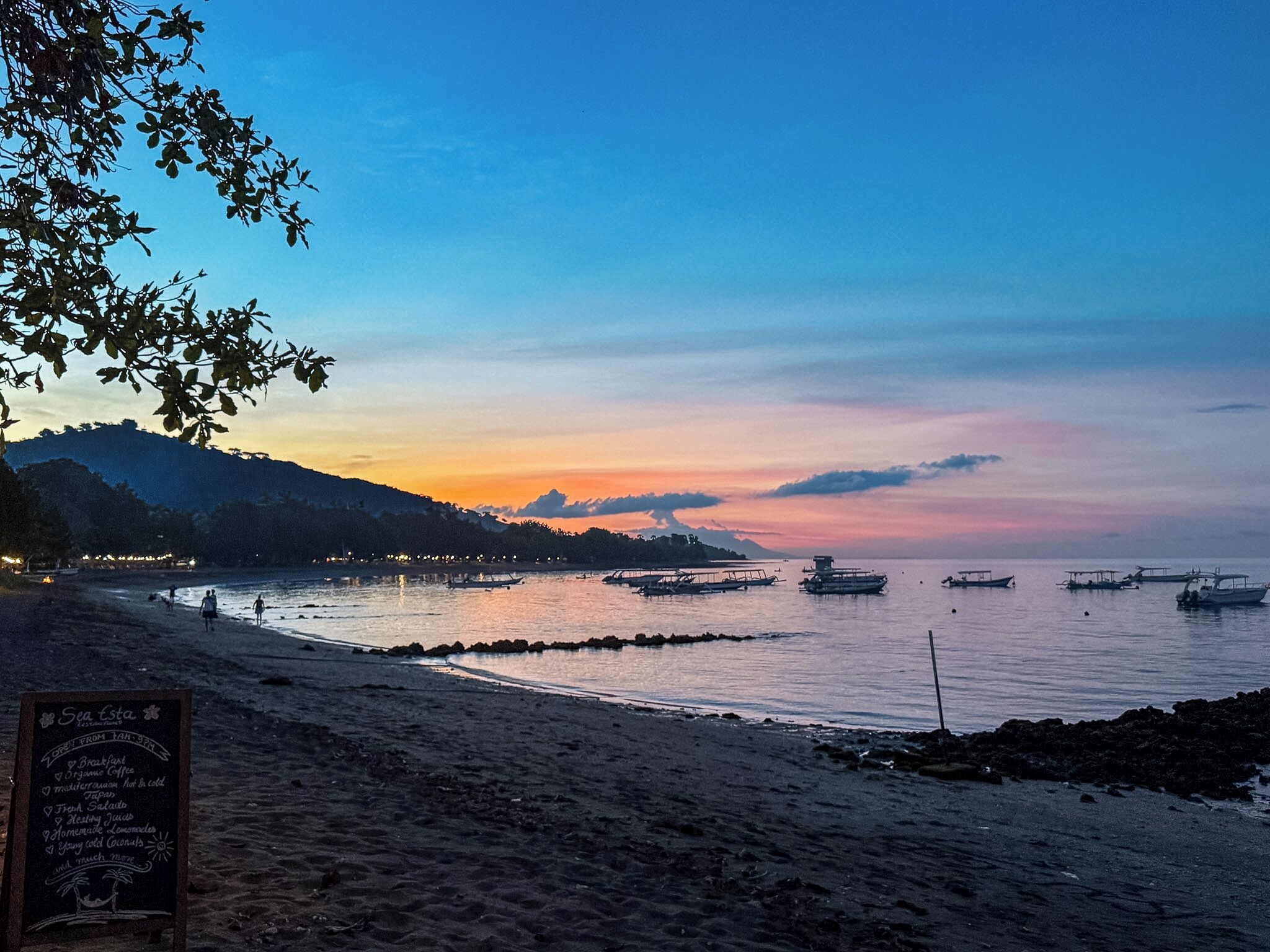 A beach with boats, a signboard, and a sunset.