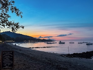A beach with boats, a signboard, and a sunset.