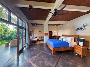 A spacious bedroom with a large bed, a ceiling fan, and a view of greenery outside.