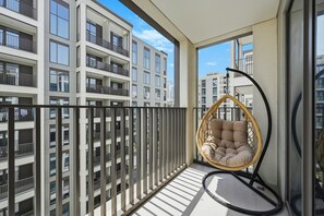 Ein Balkon mit einem Korbstuhl und Blick auf angrenzende Gebäude, der unter einem klaren Himmel liegt.