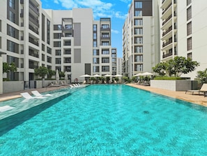 Ein Swimmingpool, umgeben von Liegestühlen und Sonnenschirmen, mit hohen Gebäuden im Hintergrund.