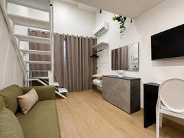 Una sala de estar moderna con un sofá, una mesita, un televisor, una escalera y un espejo.