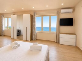 A hotel room with a bed, a TV, a wardrobe, and a view of the sea.