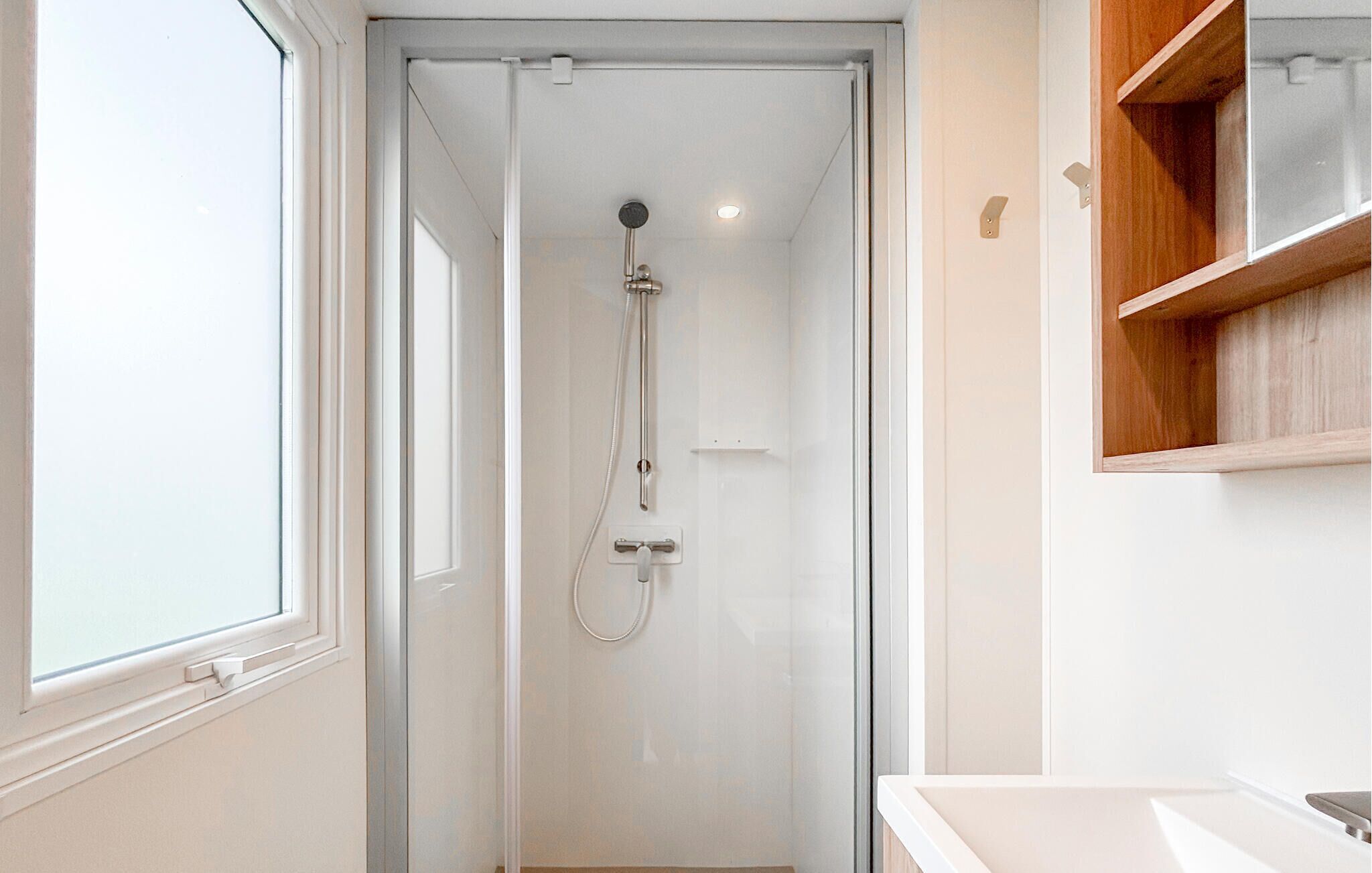 Ein modernes Badezimmer mit einer gläsernen Duschkabine, einem weißen Waschbecken und einem Holzregal.