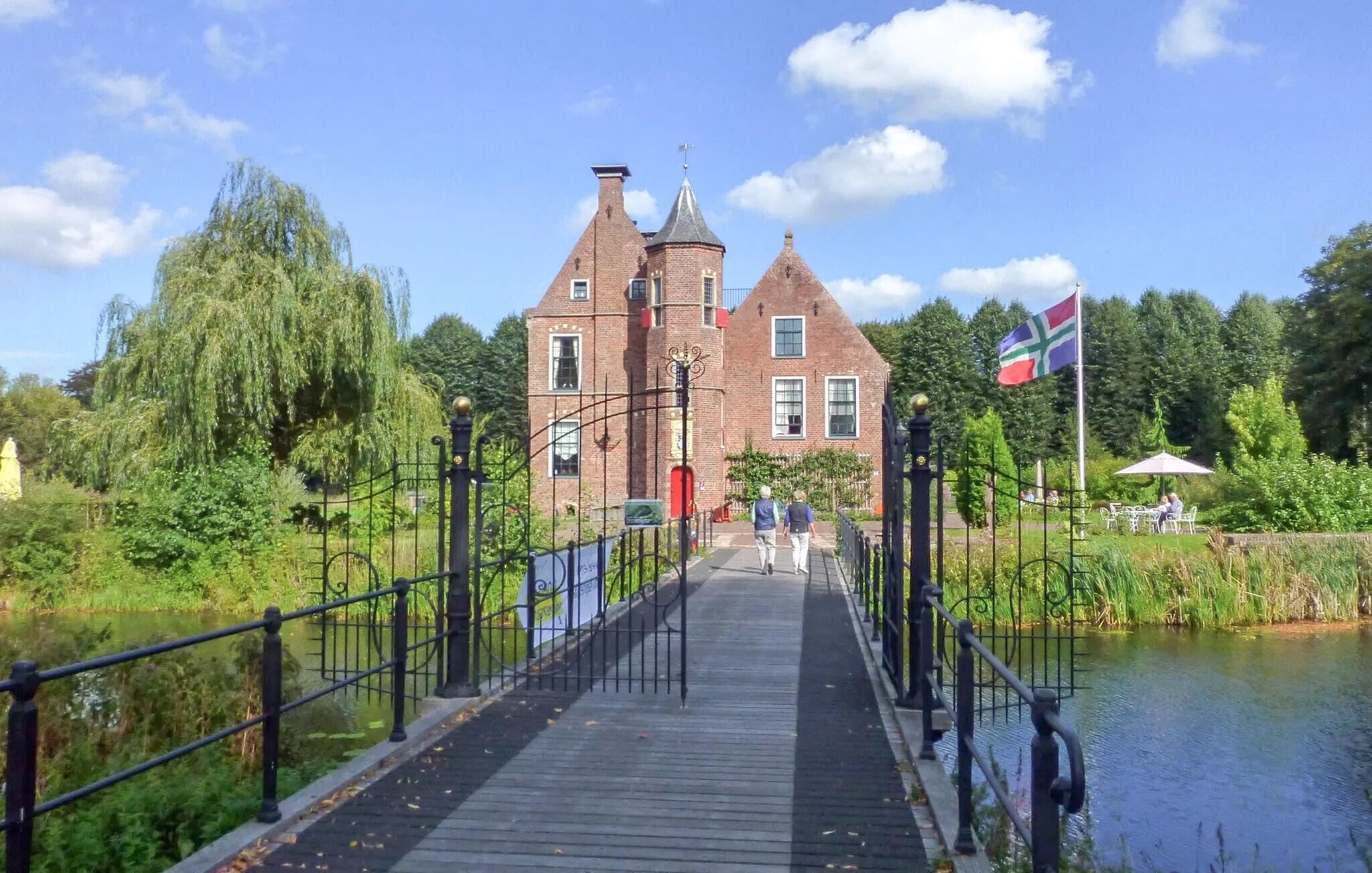 Un pont en bois mène à un bâtiment historique en briques, sur lequel flotte un drapeau.
