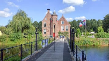 Un pont en bois mène à un bâtiment historique en briques, sur lequel flotte un drapeau.