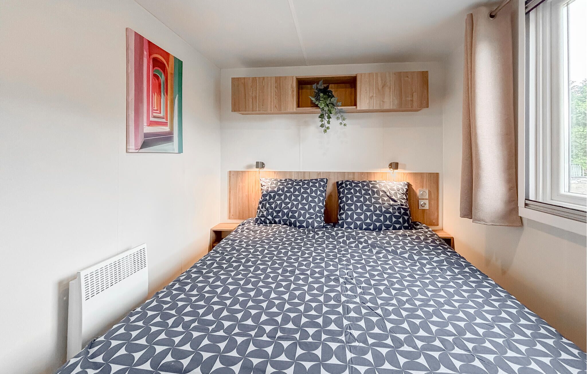 Een slaapkamer met een bed, een hoofdbord, een nachtkastje, een wandplank en een raam met gordijnen.