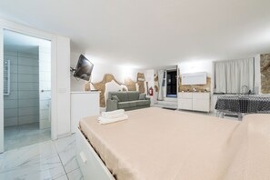 Ein modernes Hotelzimmer mit einem Bett, einer Couch, einem Fernseher und einem Badezimmer mit Dusche.