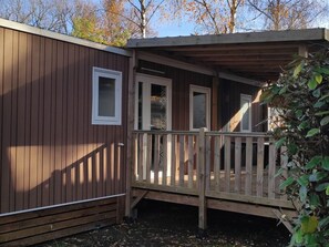 Een houten hut met een veranda en een deur naar een overdekt terras.
