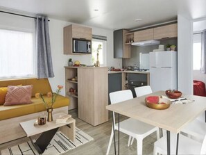 A compact living space with a kitchenette, a dining area, and a sofa with cushions. - Mobile home with AC & pets - 4 guests (Grayan-et-l'Hôpital)