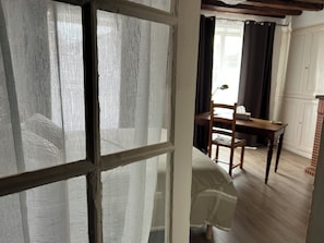 A room with a wooden floor, a dining table with chairs, and a window with a white frame and a mesh screen. - "Chez Laurette"—a vacation rental for 8 people between Beauval, Chambord, and Cheverny (Les Montils)