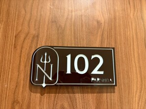 Un senyal amb números i lletres negres sobre fusta, amb el número '102' i la paraula 'PARSHWA'.