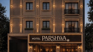 A hotel named PARSHWA with a modern facade, multiple windows, and outdoor seating area.