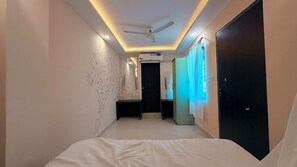 A hotel hallway with a bed, a ceiling fan, and a door leading to another room. - Hotel Parshwa (Ujjain)