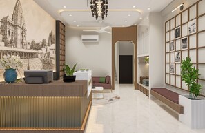 A hotel lobby with a reception desk, seating area, and a wall with framed pictures. - Hotel Parshwa (Ujjain)