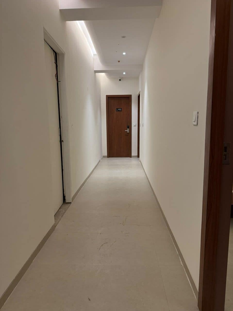A corridor with a door at the end, a light switch on the wall, and a ceiling light fixture.