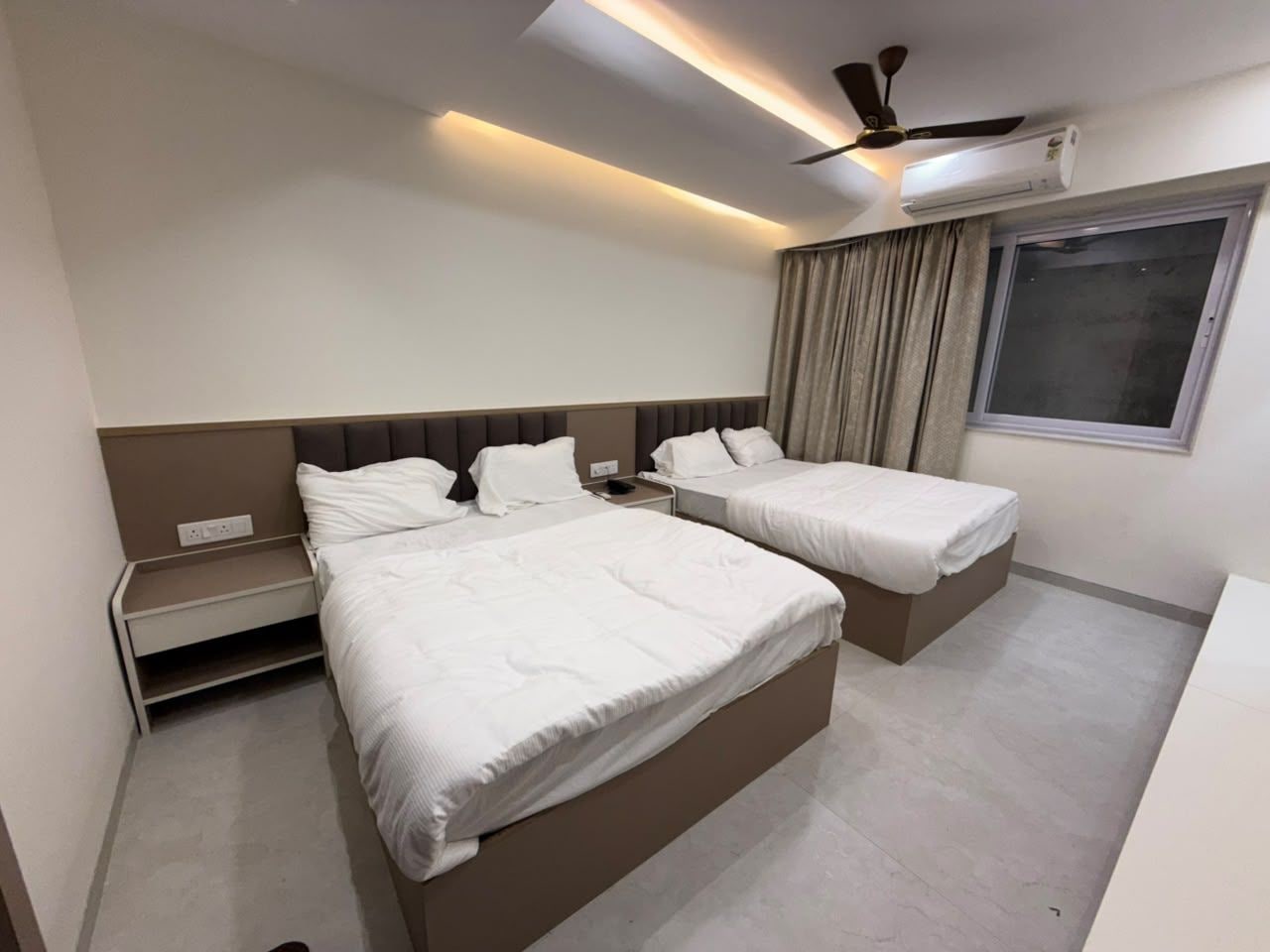 Habitación de hotel con dos camas, ventilador de techo, aire acondicionado y ventana con cortinas.