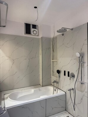 A modern bathroom with a freestanding bathtub, a showerhead, and a wall-mounted speaker. - Hotel Parshwa (Ujjain)