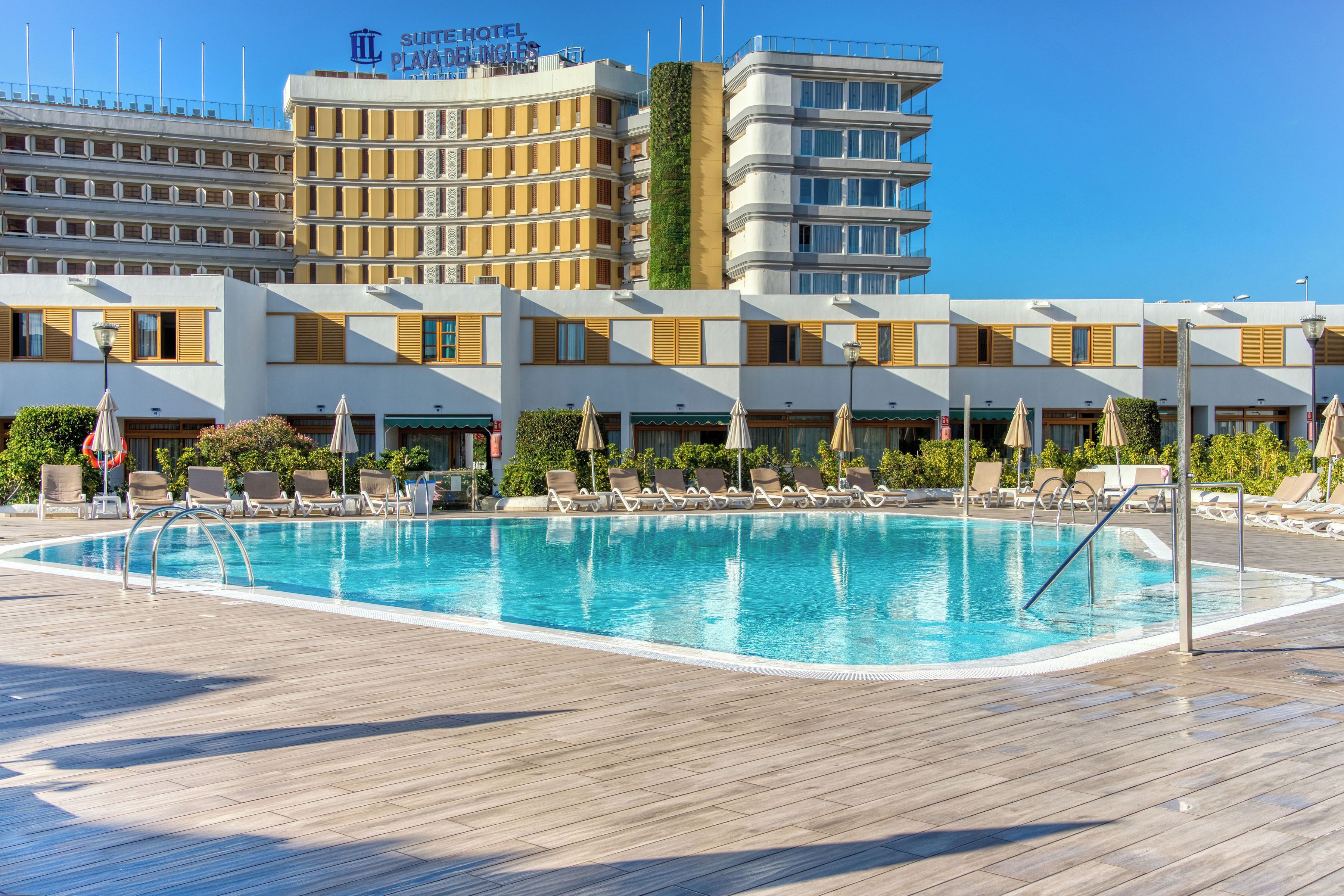 Un hotel con piscina, tumbonas y un cielo azul despejado.