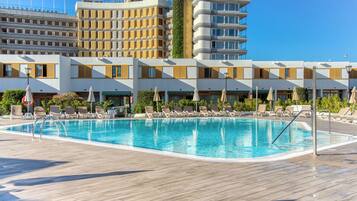 Un hotel con piscina, tumbonas y un cielo azul despejado.