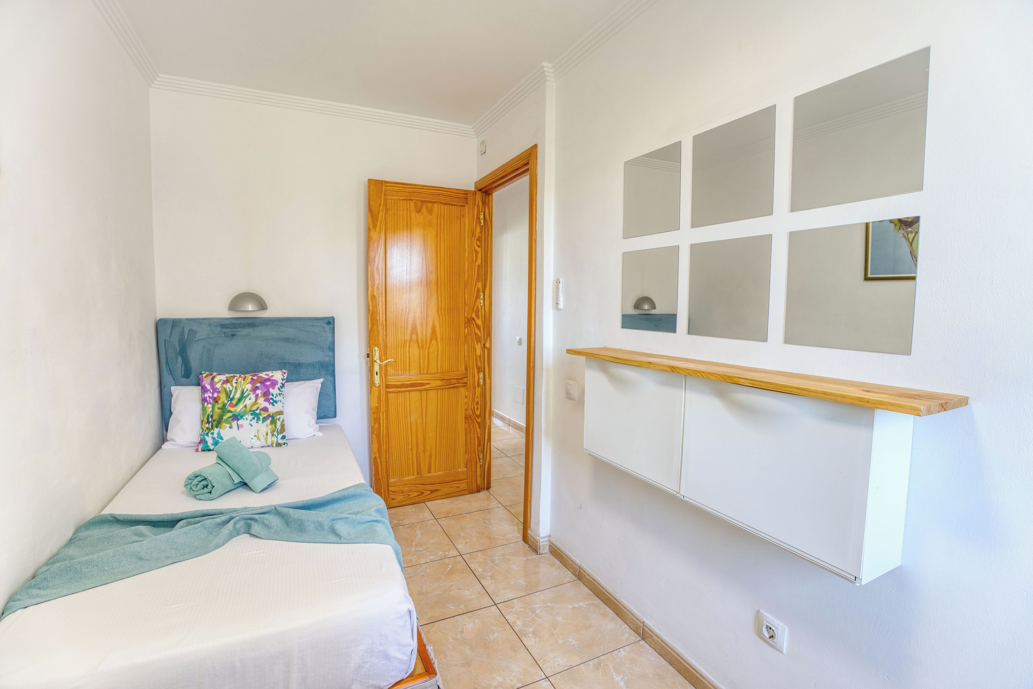 Een slaapkamer met een bed, een houten deur, een wandplank en een betegelde vloer.