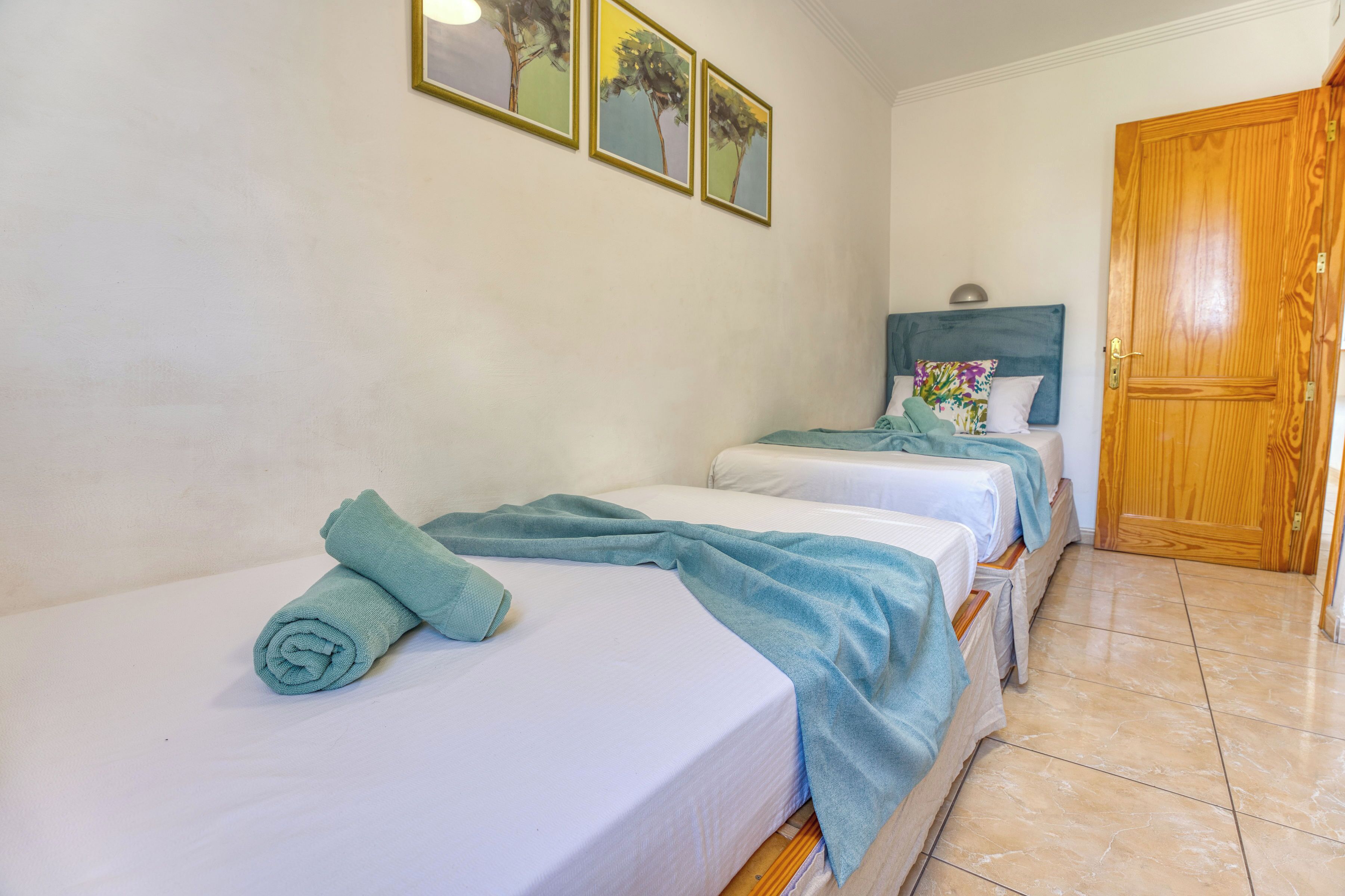 A hotel room with two single beds, a wooden door, and three wall-mounted paintings.