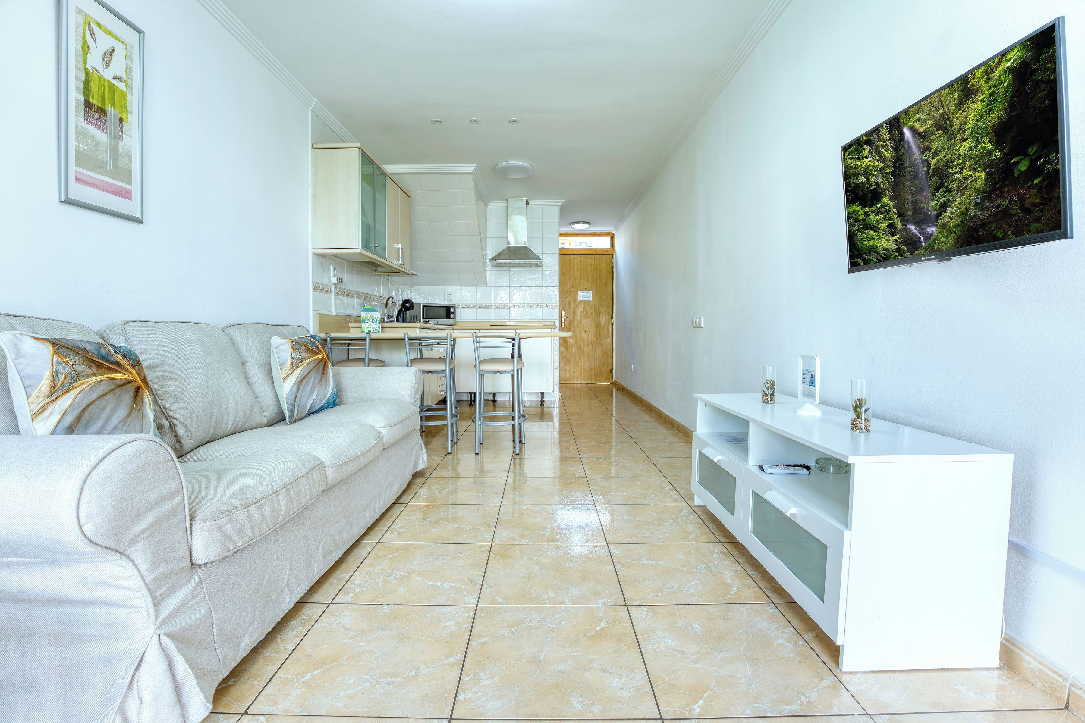 Una sala de estar moderna con un sofá, un comedor con una mesa y sillas, y una cocina al fondo.