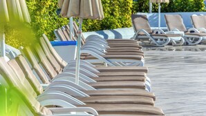 A row of sun loungers with umbrellas, a poolside area, and greenery in the background. - Las Brisas (San Bartolomé de Tirajana)