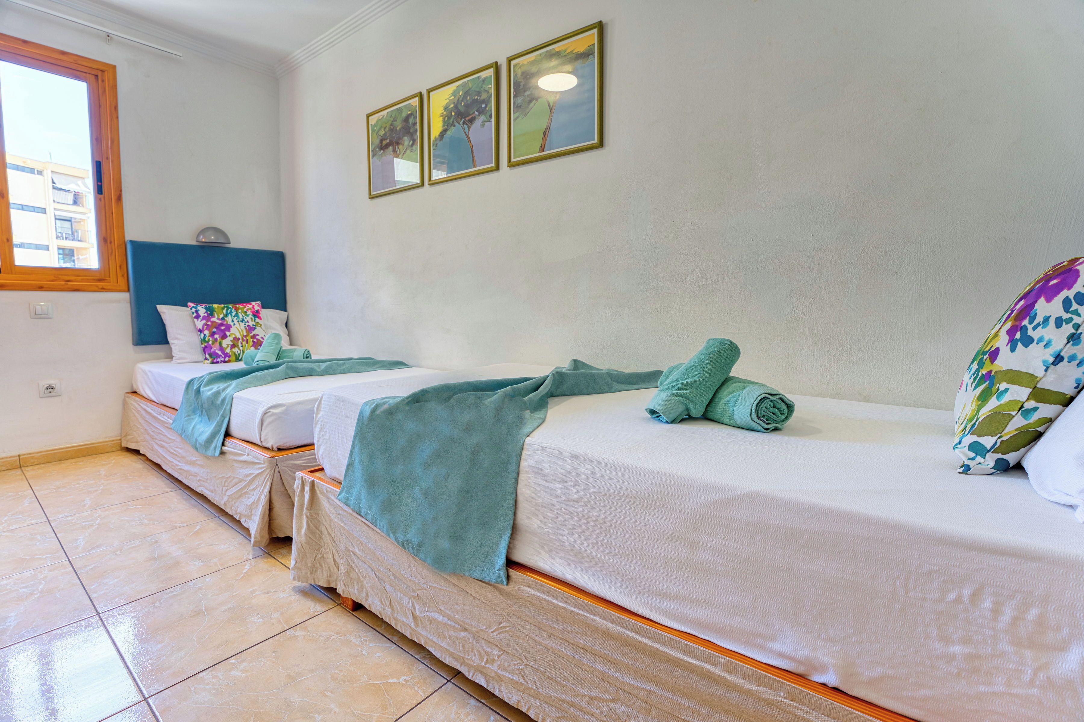 Habitación de hotel con dos camas, una ventana y tres cuadros en la pared.