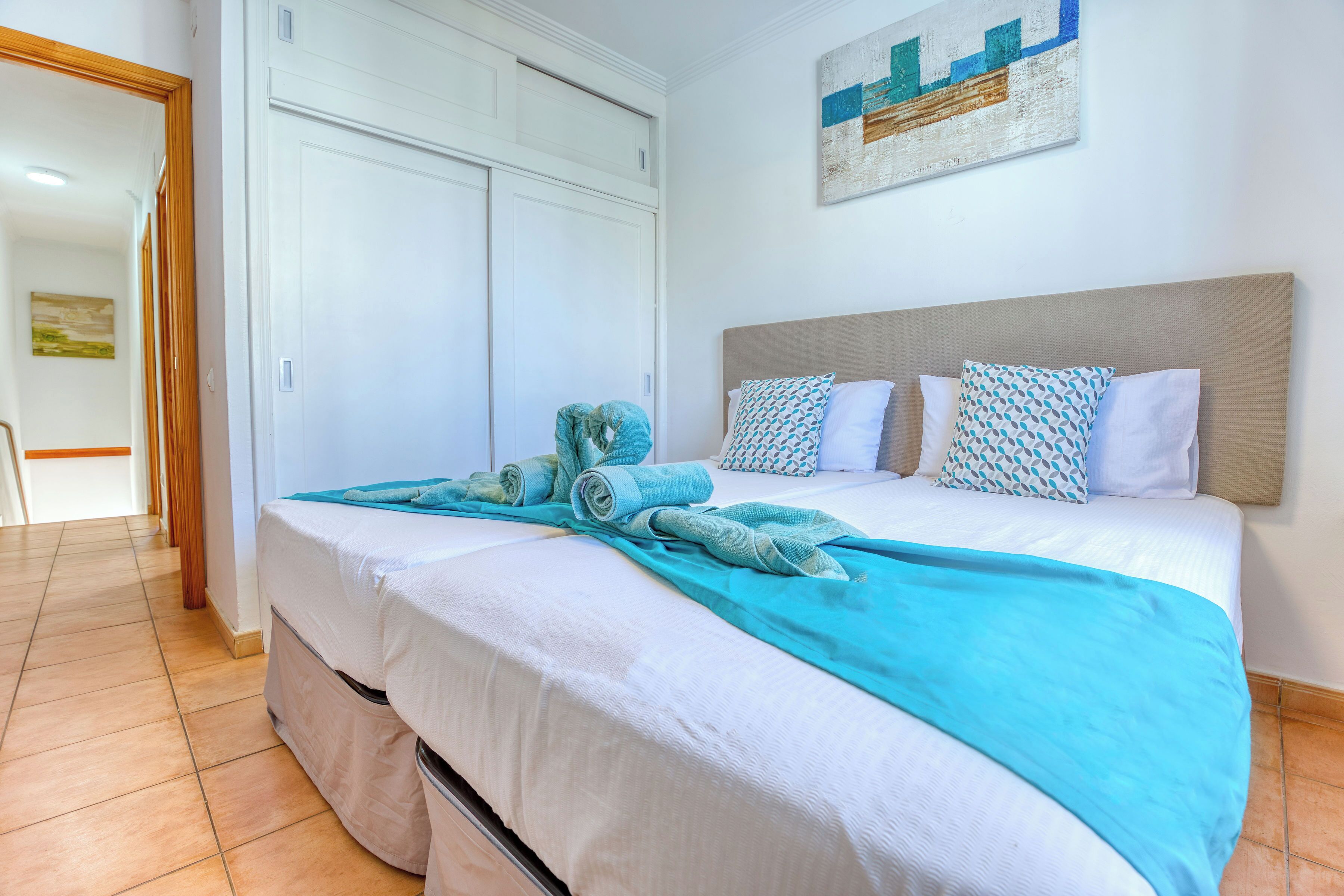 Una cama bien hecha con una colcha blanca y azul, un cabecero y varias almohadas.