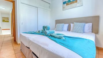 Una cama bien hecha con una colcha blanca y azul, un cabecero y varias almohadas.