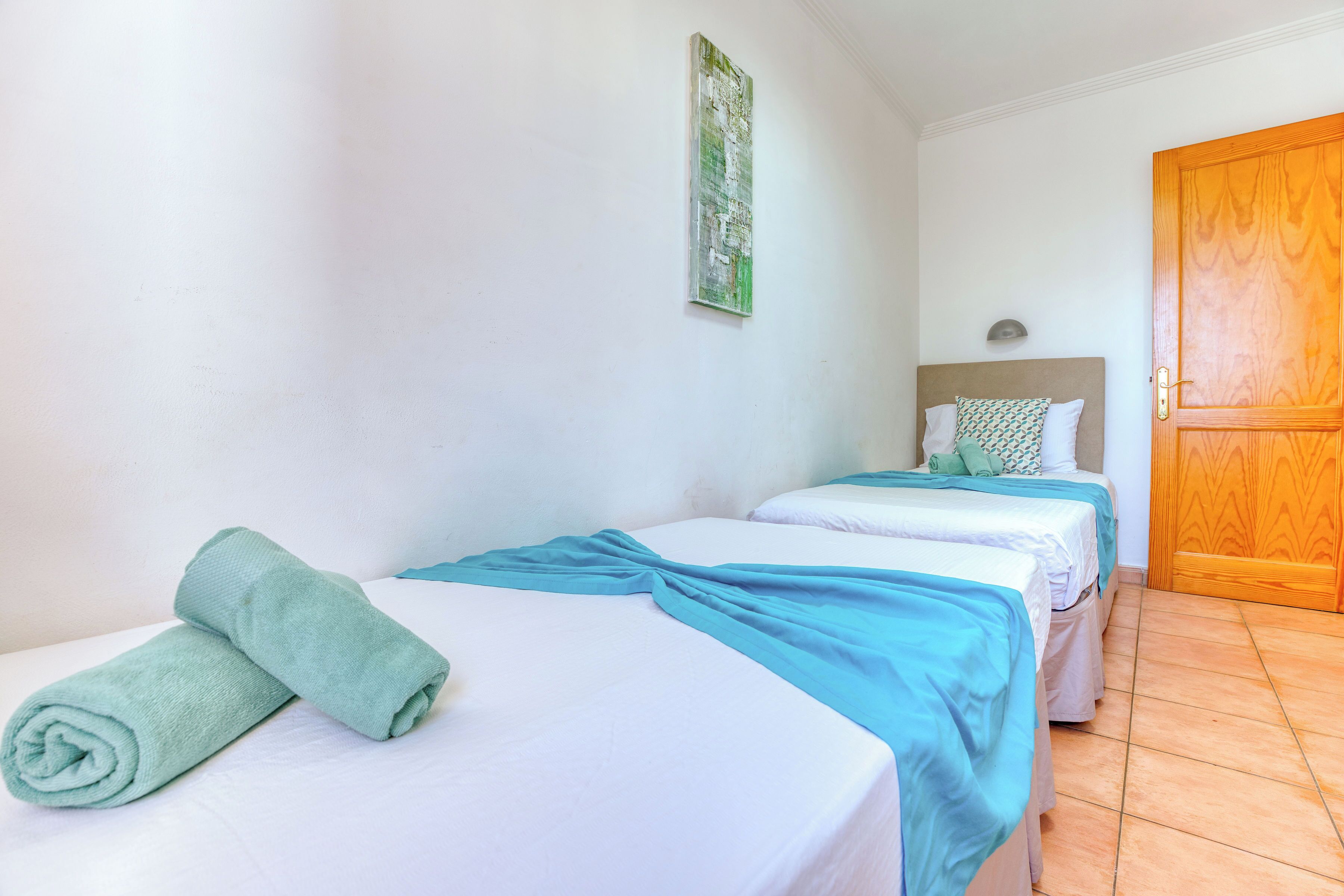 A hotel room with two beds, a wooden door, and a wall-mounted light fixture.