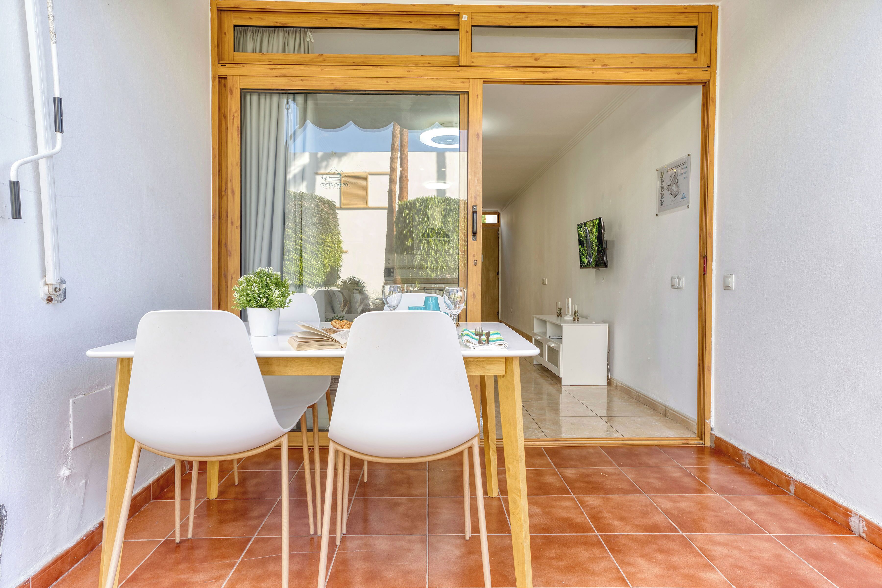Un'area pranzo con tavolo e sedie, una pianta in vaso e vista attraverso una porta in vetro.