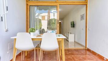 Un'area pranzo con tavolo e sedie, una pianta in vaso e vista attraverso una porta in vetro.