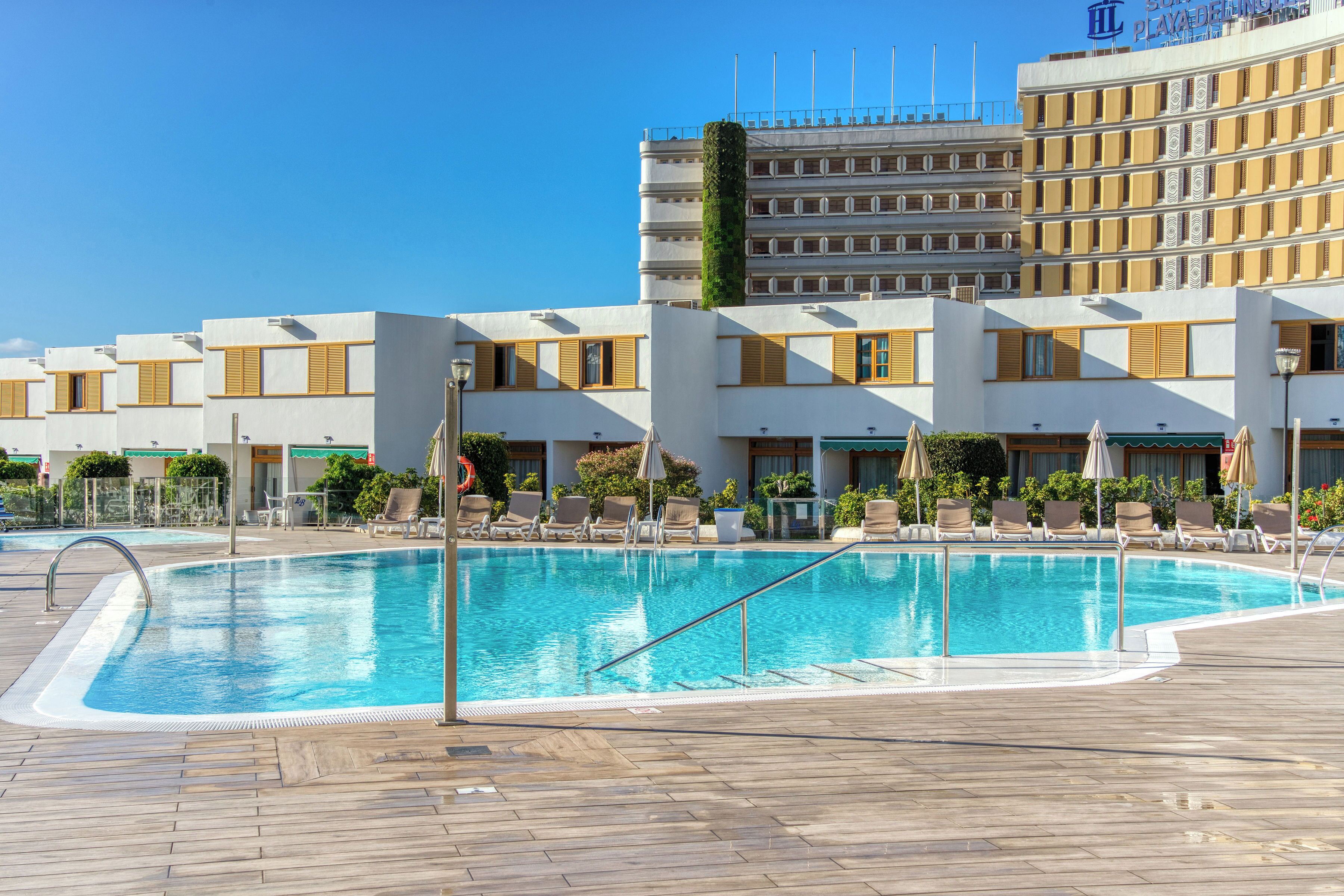A swimming pool with lounge chairs and a hotel building in the background.