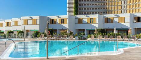 A swimming pool with lounge chairs and a hotel building in the background.