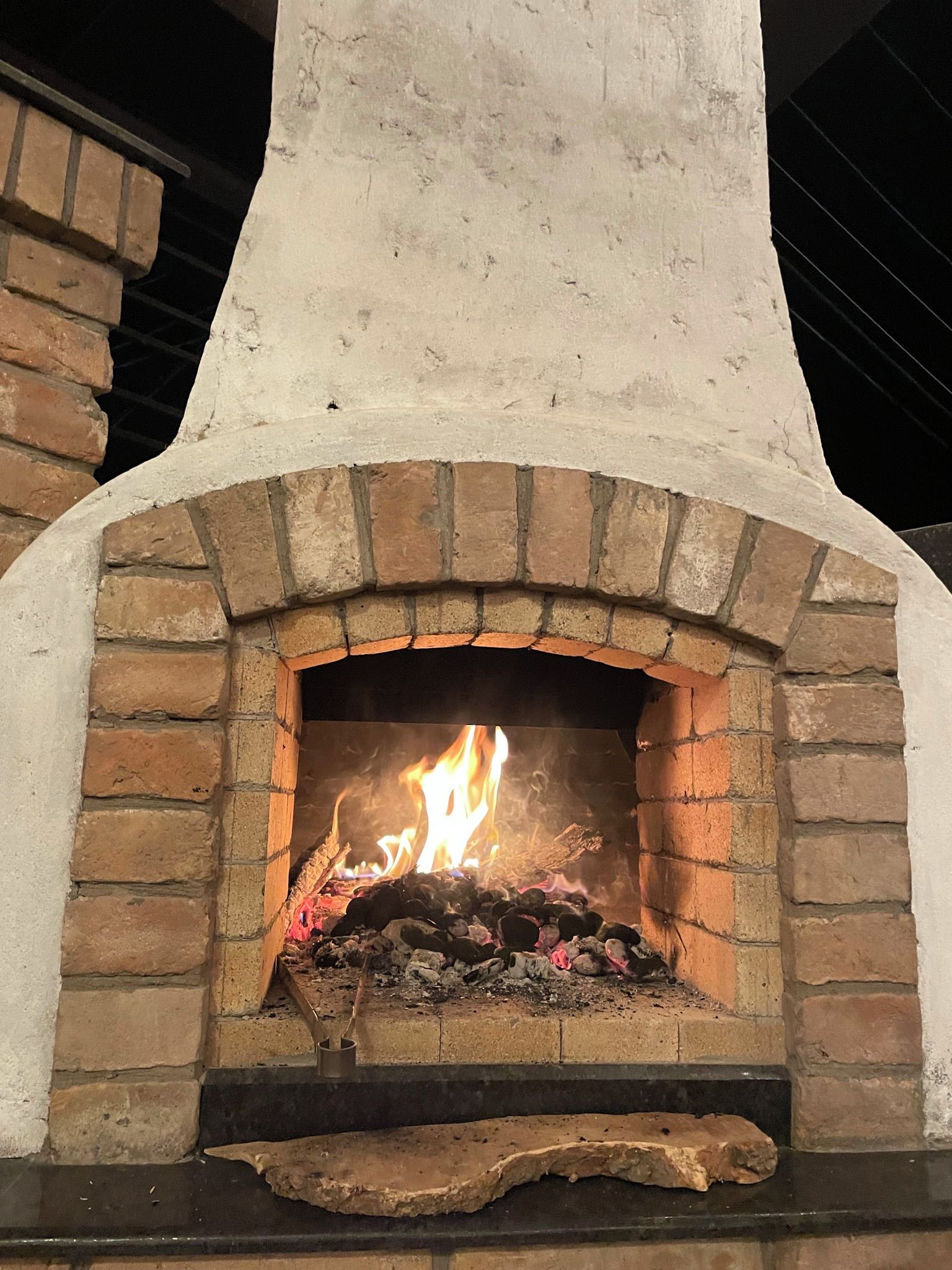 A brick fireplace with a fire burning inside, surrounded by a white mantel and a stone base.