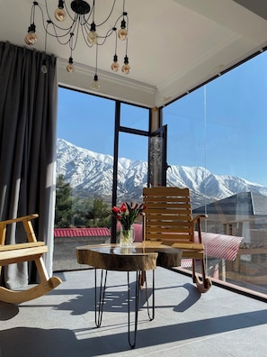 A balcony with a wooden table, chairs, and a vase of flowers. A mountain view is visible through the large windows. - Balandda Chimgan (Chimgan)