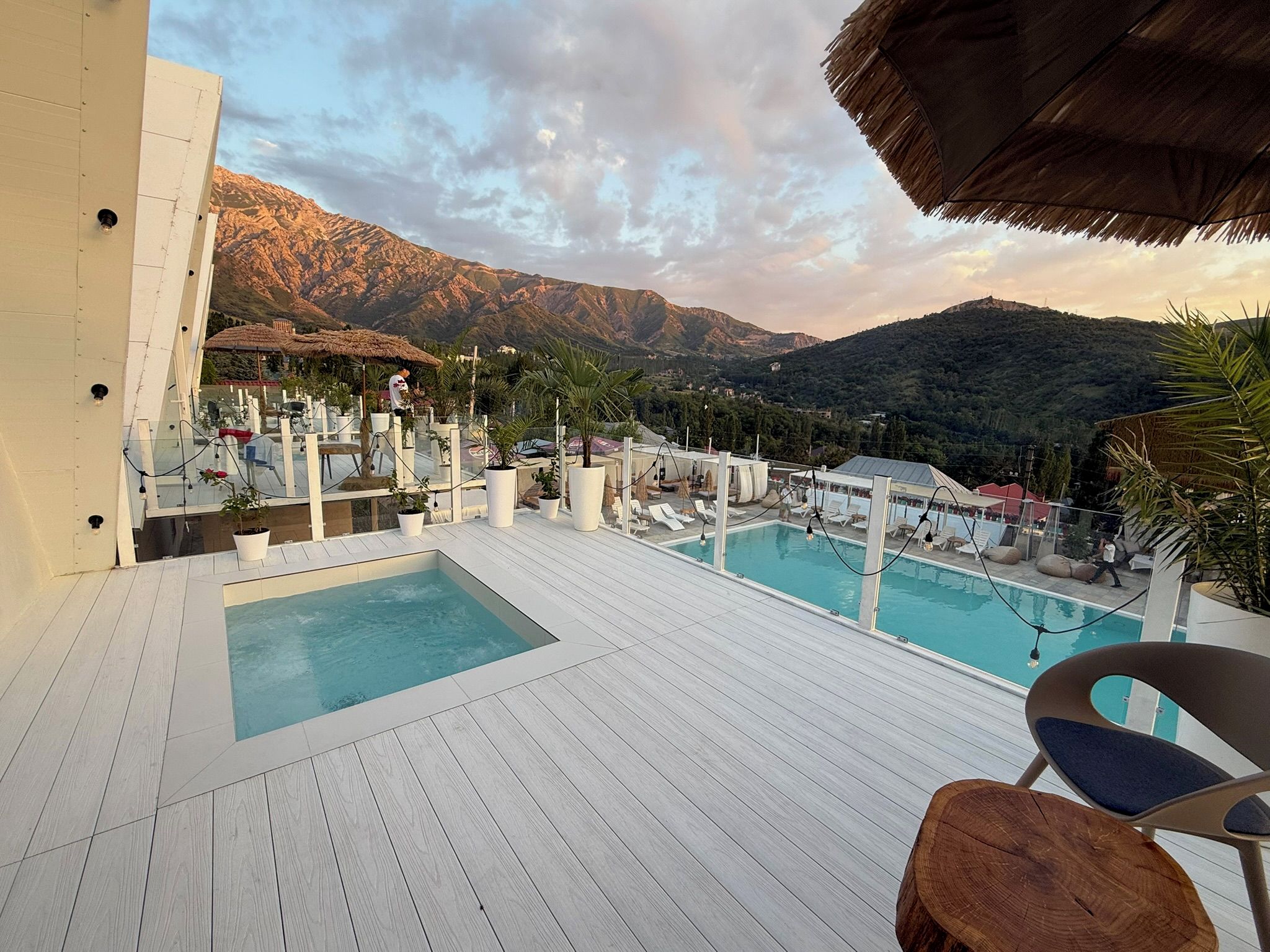 A pool area with a mountain view, lounge chairs, and a thatched roof structure.