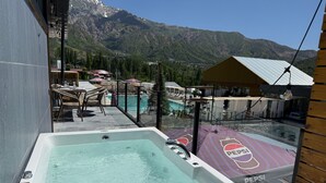 Een hottub met uitzicht op bergen en een zwembadgedeelte met parasols.