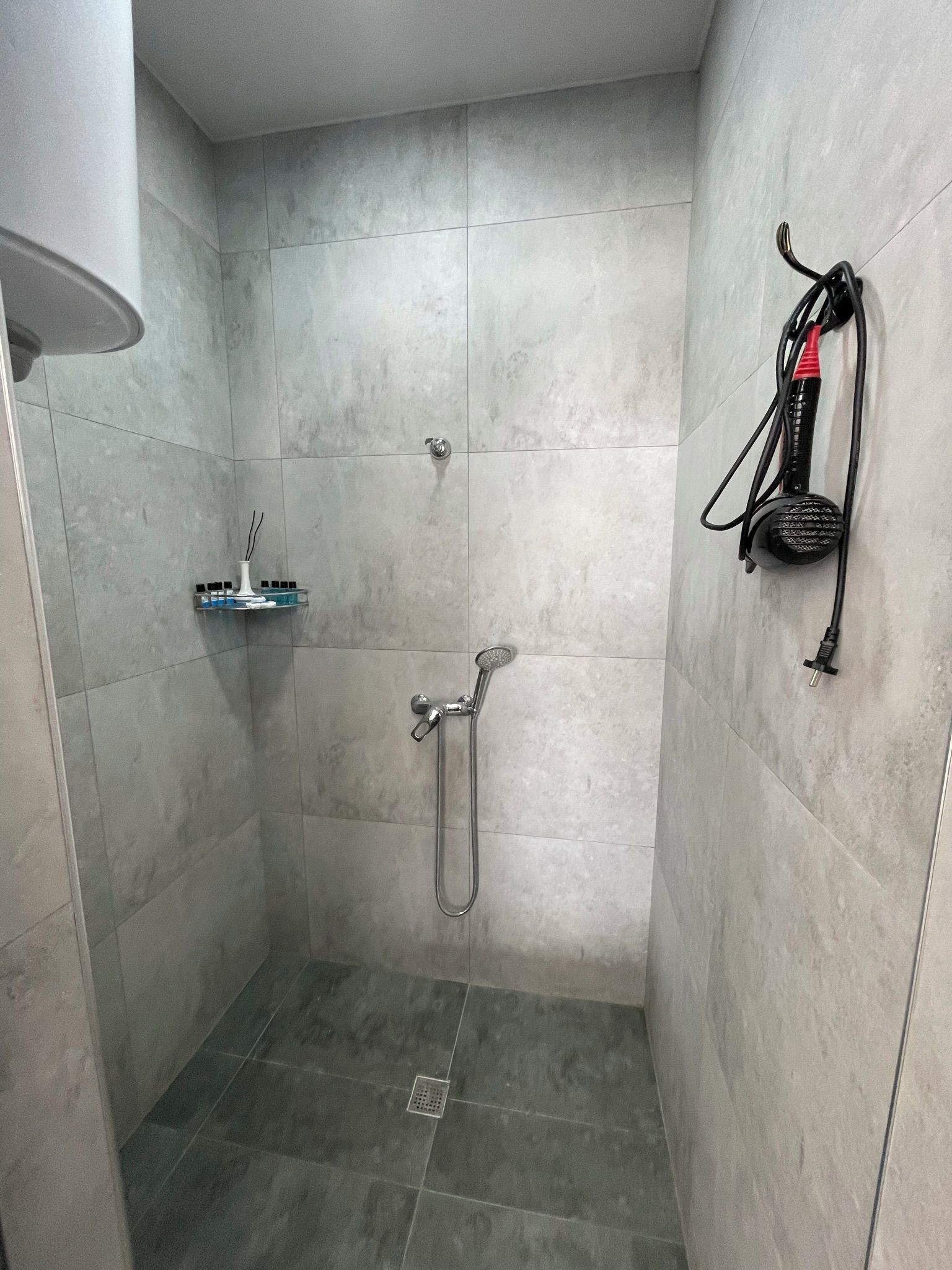 A shower area with a handheld showerhead, a wall-mounted towel rack, and a small shelf with toiletries.