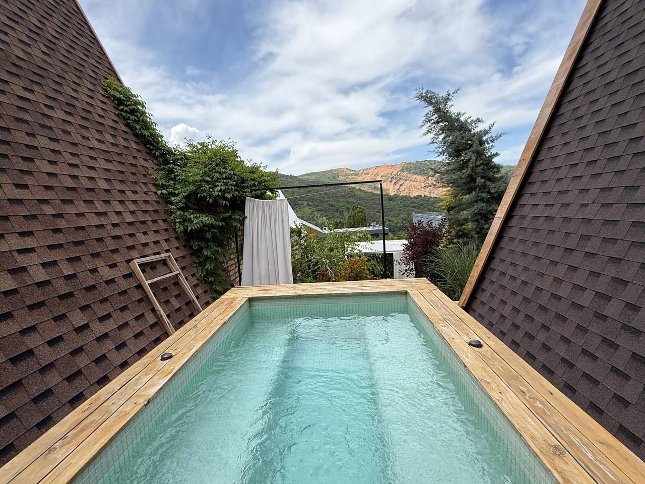 Una piscina rectangular con una terraza de madera, rodeada por una zona con techo oscuro.