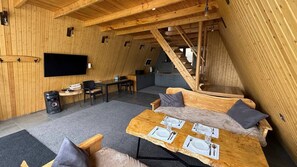 A cozy wooden interior with a dining table set for four, a sofa, a TV mounted on the wall, and a staircase leading to an upper level. - Balandda Chimgan (Chimgan)