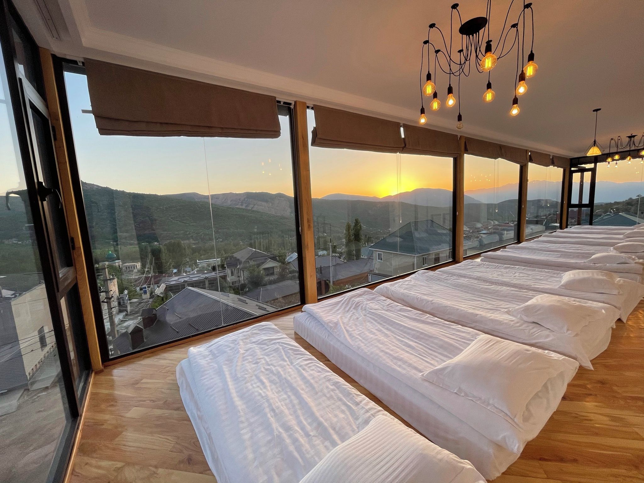 A hotel room with a large bed, multiple windows, and a view of the landscape.