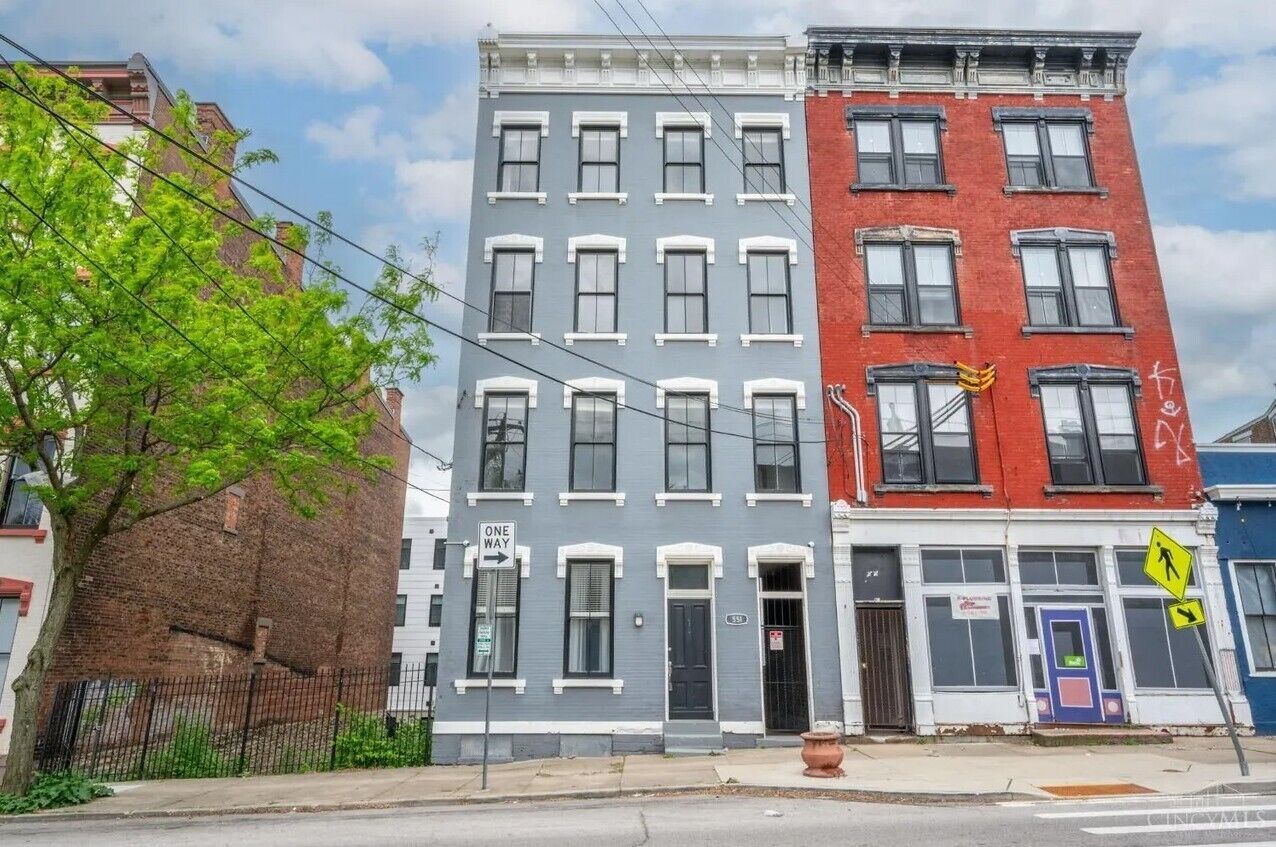 A row of multi-story buildings with a 'ONE WAY' sign, a pedestrian crossing sign, and a 'NO PARKING' sign.