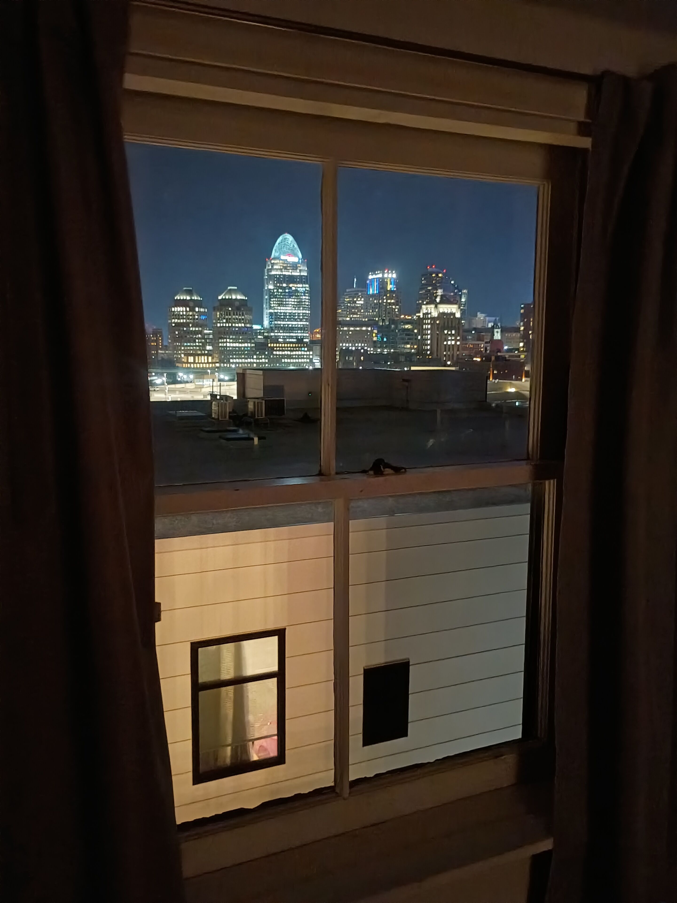 A view from a window overlooking a city skyline at night with buildings illuminated.