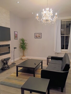 A modern living room with a flat-screen TV, a chandelier, a sofa, and a coffee table. - Edge of Downtown Cincinnati Two Floor Condo (Cincinnati)